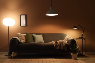 Şık oturma odasının içinde rahat kanepe, çiçek ve parlayan lambalar var.