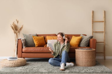 Oturma odasında tablet bilgisayar ve kulaklıkla yerde oturan genç bir kadın.