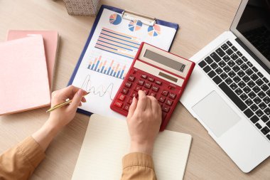 Ofiste hesap makinesi, not defteri, dizüstü bilgisayarı ve finansal grafikleri olan kadın muhasebeci