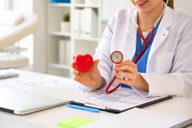 Ofisteki masasında kalbi ve steteskopu olan kadın doktor, yakın plan.
