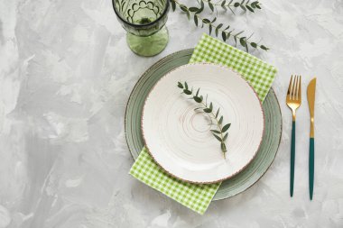 Altın çatal bıçak seti ve gri arka planda okaliptüs dalları olan güzel bir masa.