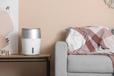 Oturma odasındaki bej duvarın yanındaki bankta hava nemlendirici.