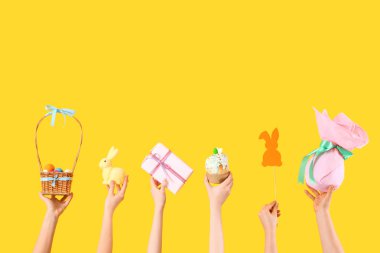 Paskalya yumurtalı kadın elleri, pasta ve sarı arka planda hediye.