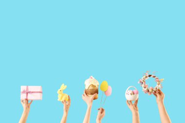 Paskalya yumurtası, pasta, çelenk ve mavi arka planda hediyeli kadın elleri.