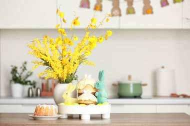 Mimoza çiçekli vazo, paskalya tavşanı ve mutfaktaki masada kek.