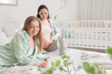 Genç hamile çift yatak odasında dizüstü bilgisayar kullanıyor.