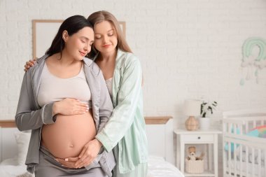 Genç hamile lezbiyen çift yatak odasında sarılıyor.