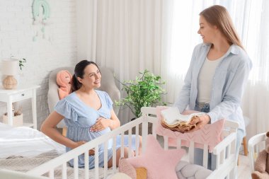 Yatak odasında bebek kıyafetleri olan genç hamile lezbiyen çift.