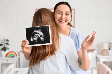 Sonogram görüntüsü olan genç hamile lezbiyen çift yatak odasında sarılıyorlar.
