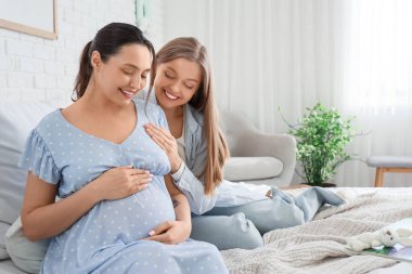 Genç hamile lezbiyen çift yatak odasında oturuyor.