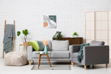 Oturma odasının içinde gri kanepe, koltuk ve yeşil bitkiler var.