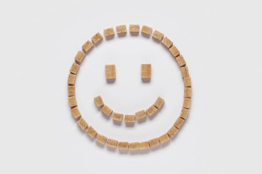 Beyaz arkaplanda kahverengi şeker küplerinden yapılmış bir gülümseme