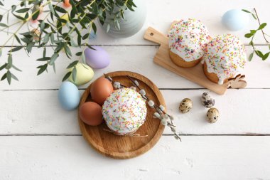 Sweet Easter cakes with different eggs and pussy willow branches on white wooden background