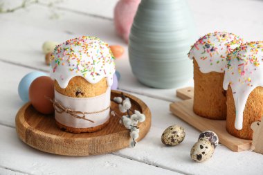 Sweet Easter cakes with different eggs and pussy willow branches on white wooden background