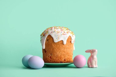 Tatlı Paskalya pastalı tabak, turkuaz arka planda boyanmış yumurta ve oyuncak tavşan.