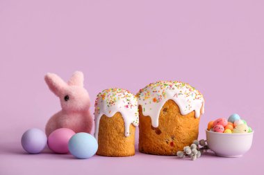 Sweet Easter cakes with painted eggs, toy bunny and pussy willow branches on lilac background