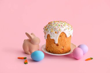 Tatlı Paskalya pastalı tabak, pembe arka planda boyanmış yumurta ve oyuncak tavşan.