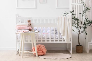 Bebek odasının içinde beşik, katlanan perde ve bebek kıyafetleri var.