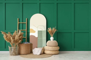 Ayna, sepet ve otlar yeşil duvarın yanında.