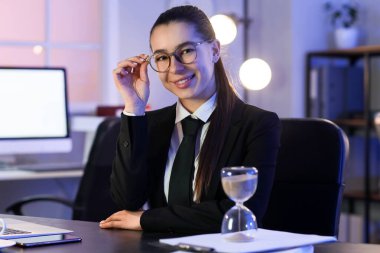 Genç iş kadını akşam ofiste oturuyor.