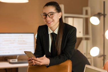 Akşam ofiste cep telefonuyla çalışan genç bir iş kadını.