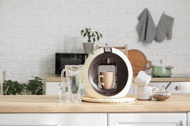 Fincanlı modern kahve makinesi, mutfakta bir sürahi su ve bir kase fasulye.