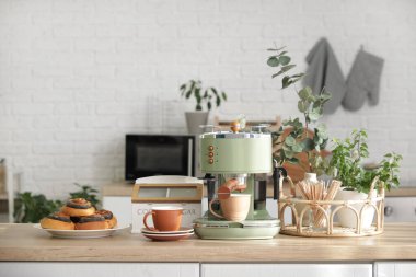 Modern kahve makinesi, fincanlar ve çörekler mutfaktaki masada.