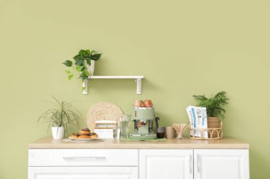 Modern kahve makinesi, fincanlar, gazete ve çörekler mutfaktaki masada.