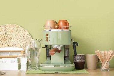 Modern kahve makinesi, fincanlar, bir sürahi su ve karıştırıcılar mutfaktaki masada.