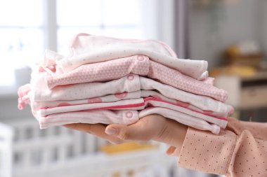 Bebek odasında yığınla bebek kıyafetleri olan kadın elleri, yakın plan.