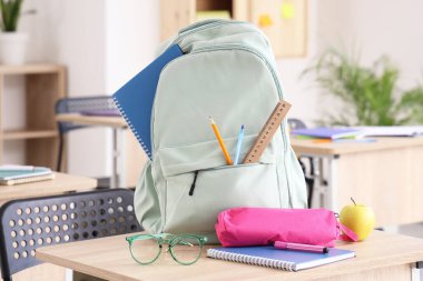 Okul kırtasiyesi ve gözlüklü sırt çantası sınıfta masanın üstünde.