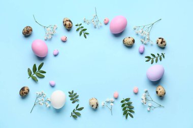 Paskalya yumurtalarından, yeşil yapraklardan ve mavi arka planda çiçeklerden yapılmış çerçeve