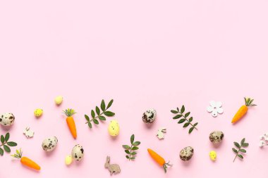 Paskalya yumurtaları, yeşil yapraklar ve pembe arka planda dekoratif havuçlar.