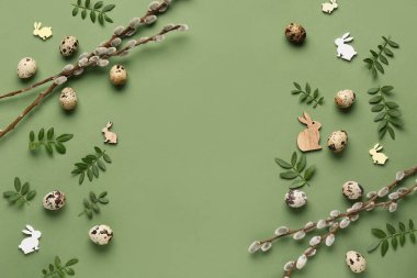 Frame made of Easter eggs, green twigs, decorative bunnies and pussy willow branches on green background