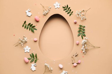 Çiçekli kompozisyon, Paskalya yumurtaları, yeşil yapraklar ve bej arka planda yumurta şeklinde boşluk.
