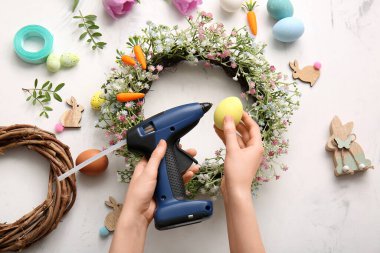 Paskalya çelengini çiçeklerle, havuçlarla ve beyaz arka planda boyanmış yumurtalarla süsleyen kadın.