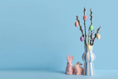 Renkli Paskalya yumurtaları ve mavi arka planda oyuncak tavşanlarla dolu söğüt ağacı dalları.