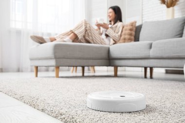 Robot süpürge halıda kadına karşı. Evde kahve içiyor, yakın plan.