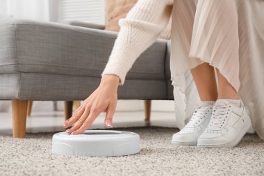 Evde robot elektrik süpürgesini açan genç bir kadın, yakın çekim.