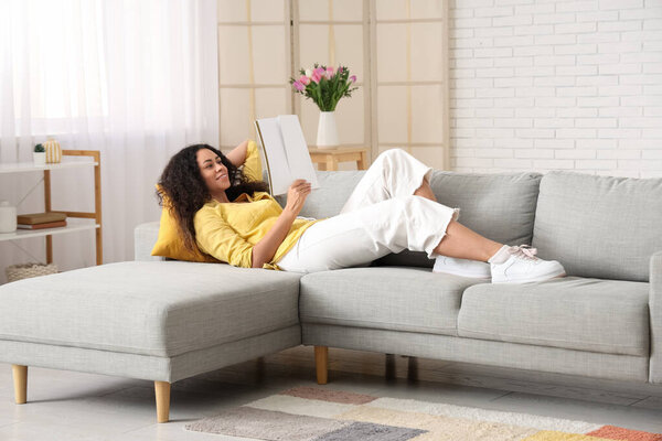 Young African-American woman reading blank magazine at home on spring day