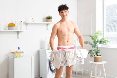 Çamaşır sepetini evde tutan külotlu genç adam.