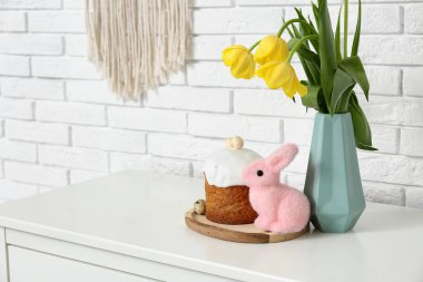 Vazoda lale çiçekleri, paskalya pastası ve beyaz tuğla duvarın yanında klozette tavşan.