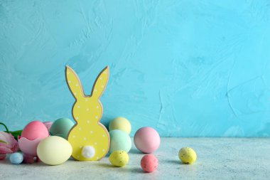 Paskalya yumurtaları ve ahşap tavşancık mavi duvarın yanındaki gri masada.