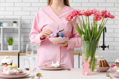 Mutfakta boyalı yumurta ve ahşap paskalya tavşanı taşıyan bir kadın. Yakın çekim.