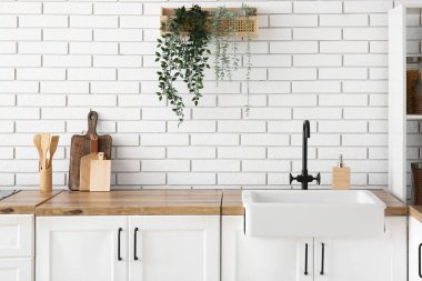 Mutfaktaki beyaz tuğla duvarın yanında lavabo ve çatal bıçaklarla tezgahlar.