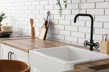 Mutfakta beyaz tuğla duvarın yanında siyah musluk olan seramik lavabo, yakın plan.