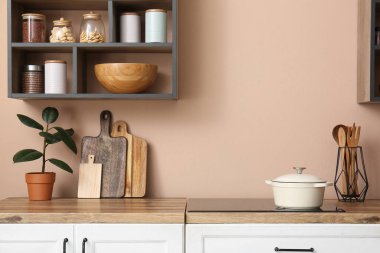 Mutfaktaki bej duvarda mutfak gereçleri ve raflarla tezgahlar.