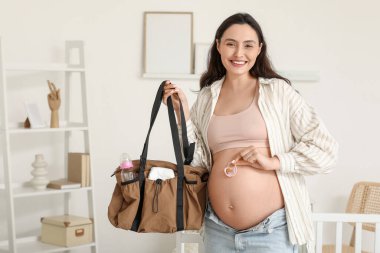 Bebek emziği ve doğum çantasıyla çocuk odasında genç hamile bir kadın.