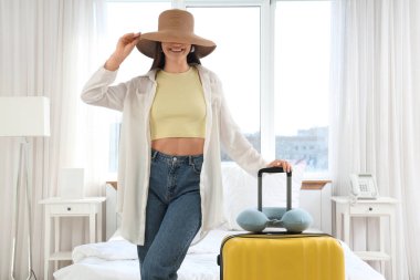 Otel odasında şapkası ve bavulu olan bir kadın turist.