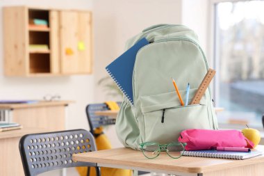 Okul kırtasiyesi ve gözlüklü sırt çantası sınıfta masanın üstünde.